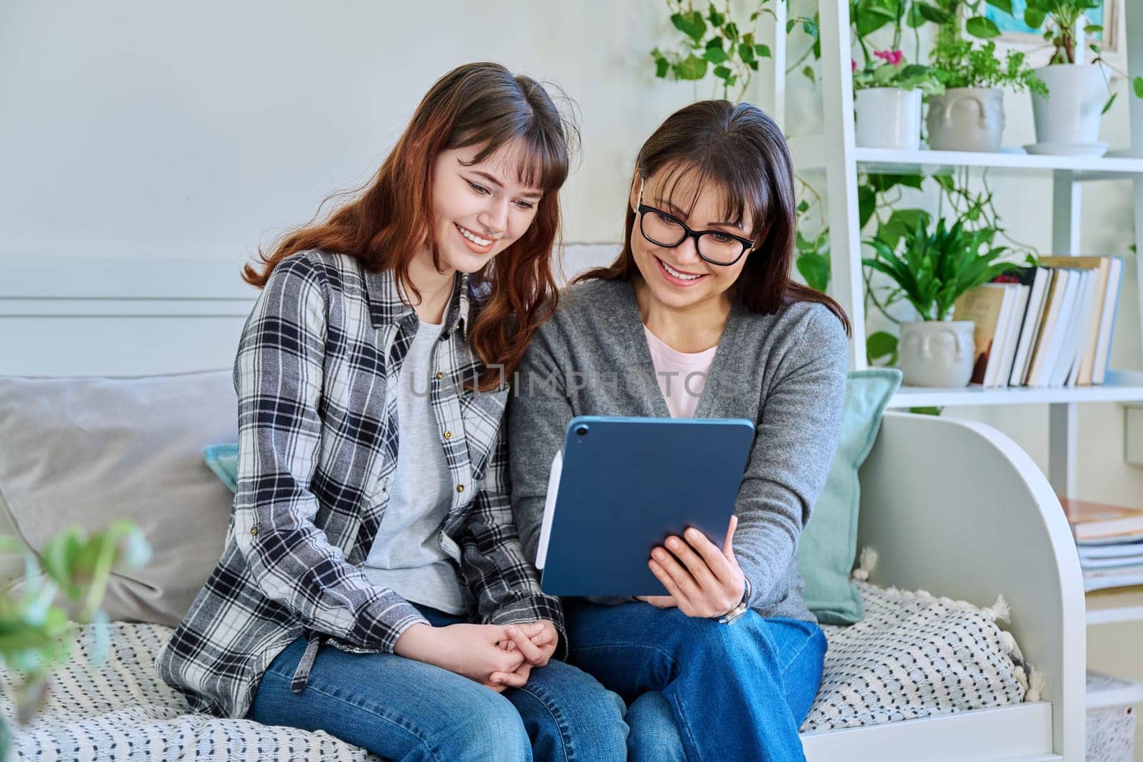 Happy talking laughing mother and teenage daughter looking together at screen of digital tablet gadget. Communication leisure shopping together watching videos chat social networks. Family friendship