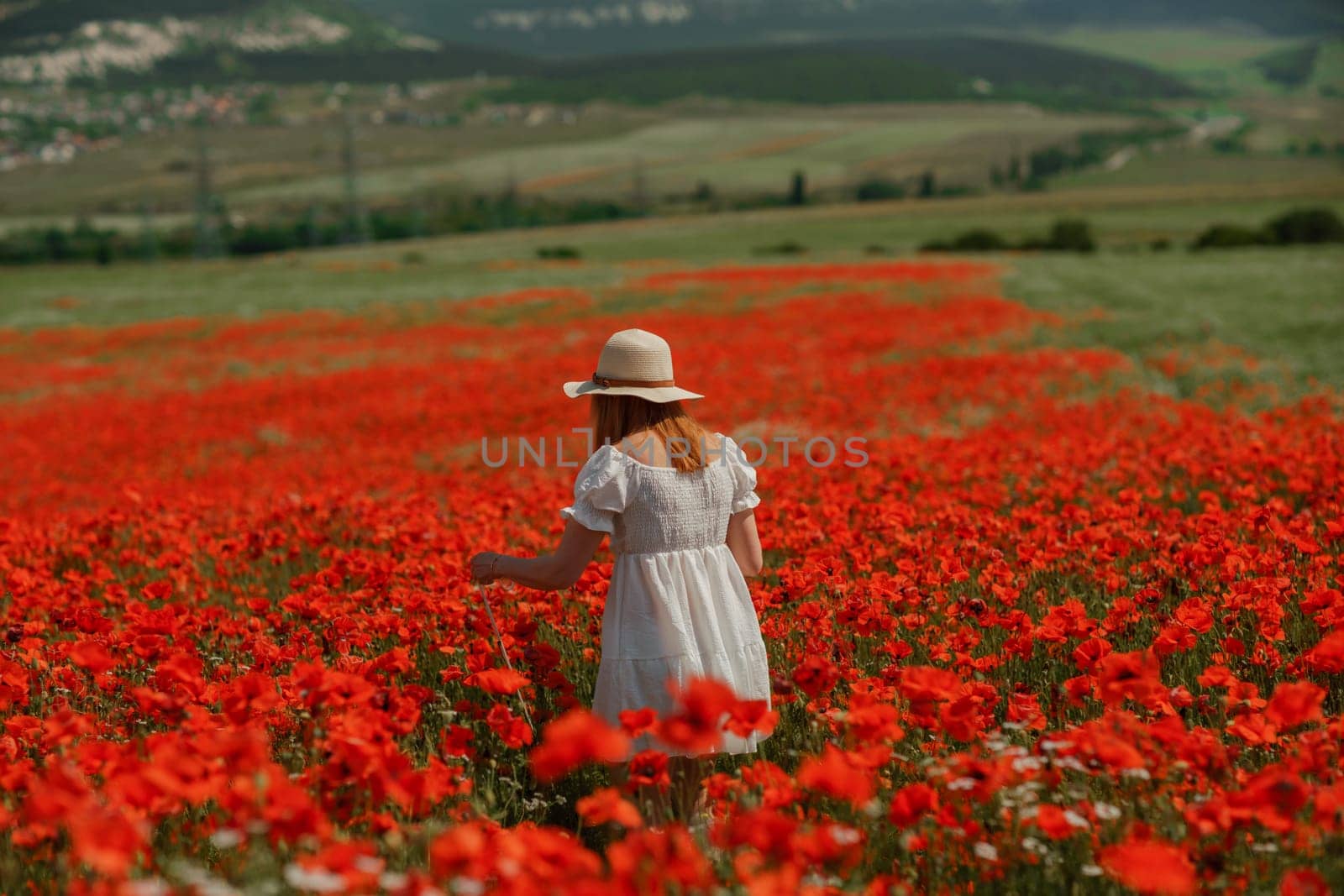 Field poppies woman. Happy woman in a white dress and hat stand with her back a blooming field of poppy. Field of blooming poppies