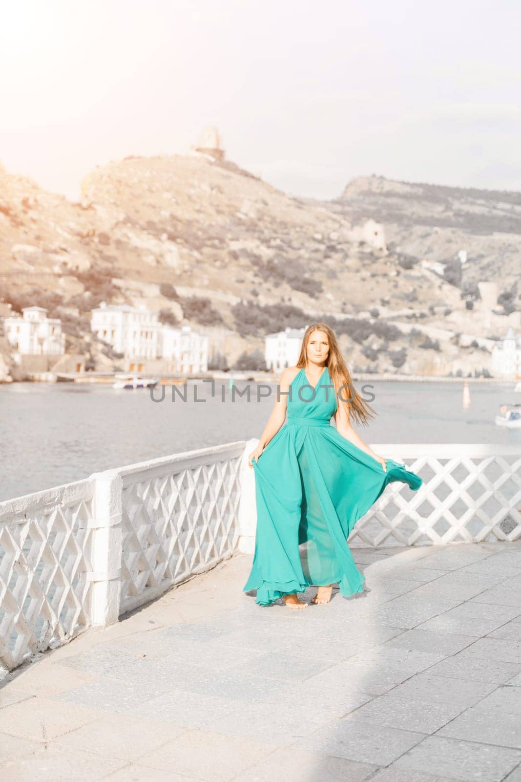 Woman sea trevel green dress. Side view a happy woman with long hair in a long mint dress posing on a beach with calm sea bokeh lights on sunny day. Girl on the nature on blue sky background