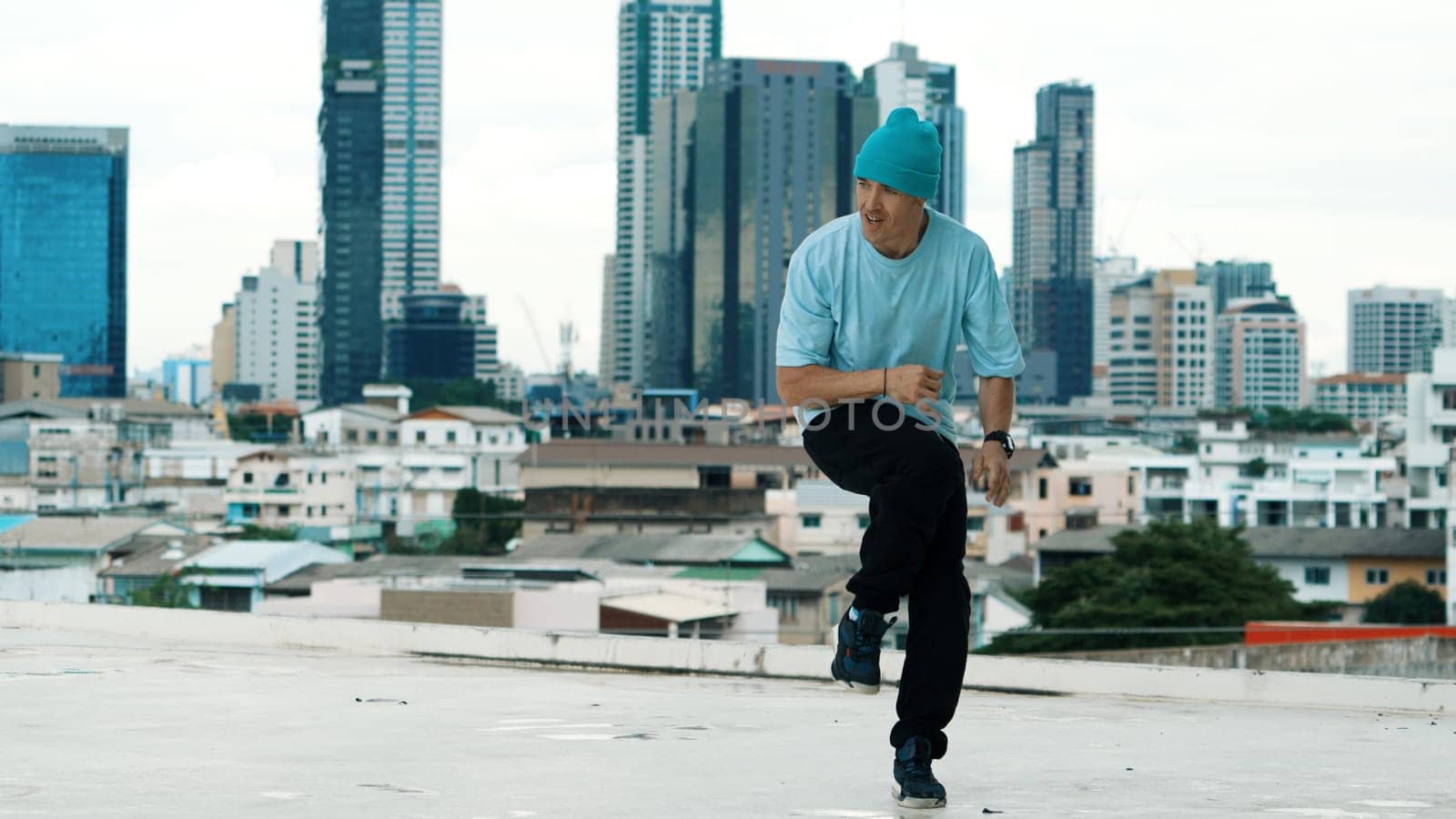 Skilled caucasian B-boy dancer practicing street dancing at rooftop with city sites or urban. Motion shot of young man performing street dance by doing freeze pose. Outdoor sport 2024. Endeavor.