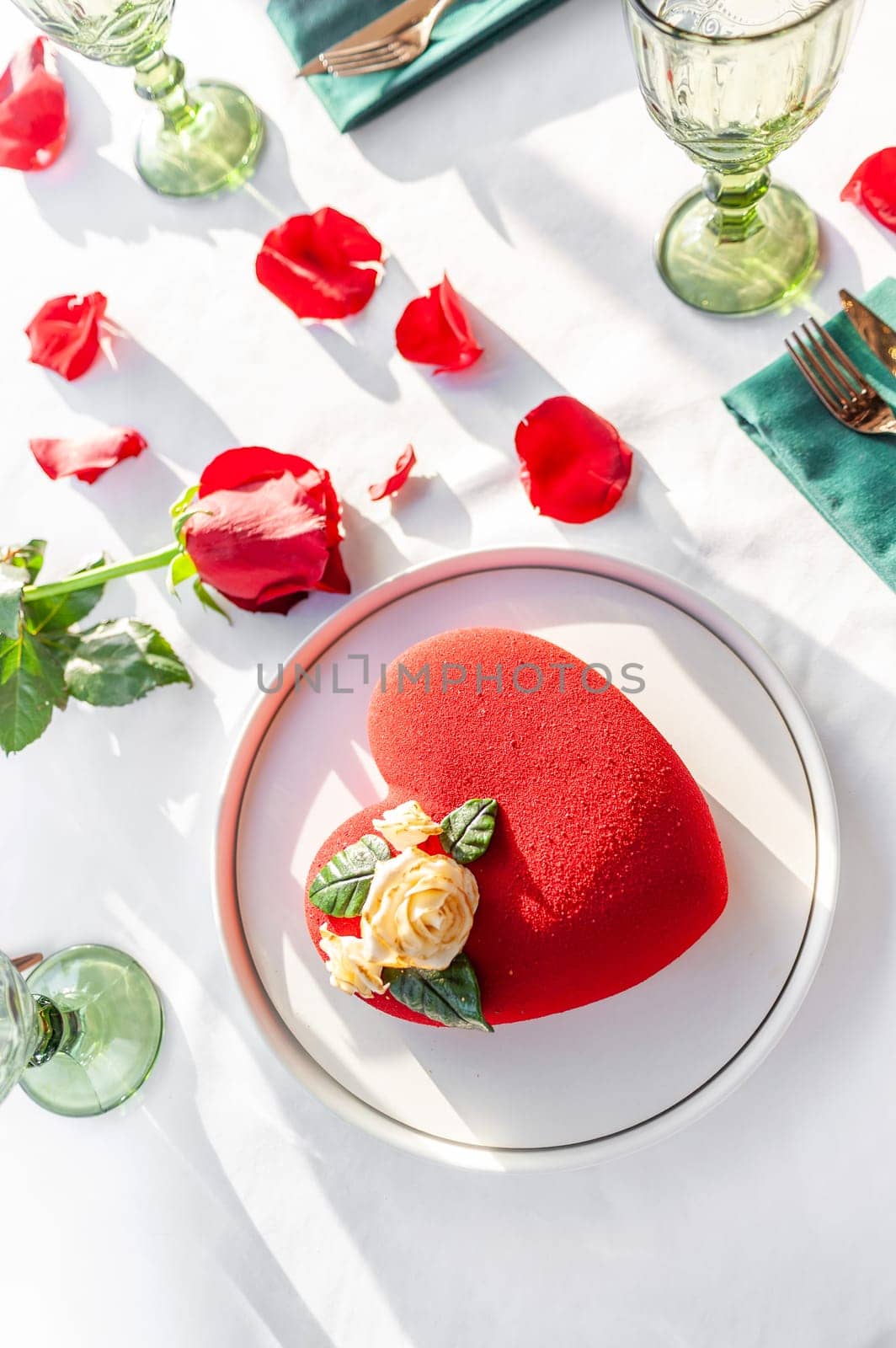 Heart Shaped Red Velvet Valentine's Day Cake on a white tablecloth with a red rose and rose petals in a restaurant. High quality photo
