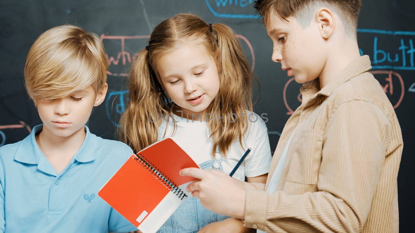 Group of caucasian student checks robotic model while taking a note.at blackboard with engineering code or prompt written. Children studying, learning about programing robot in STEM class. Erudition.