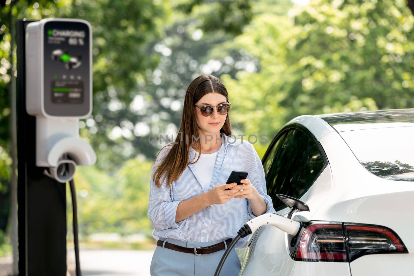 Young woman using smartphone to pay for electric car charging. Exalt by biancoblue