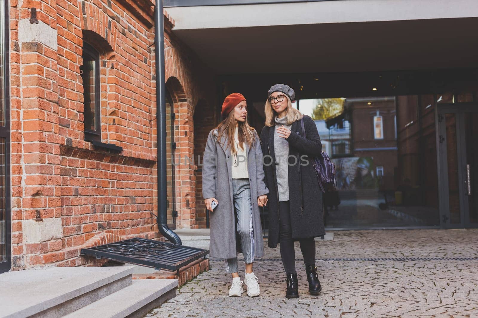 Two girls walking on street together and holding their hands. They are wearing spring or autumn clothes and they happy. Friendship and relationship concept