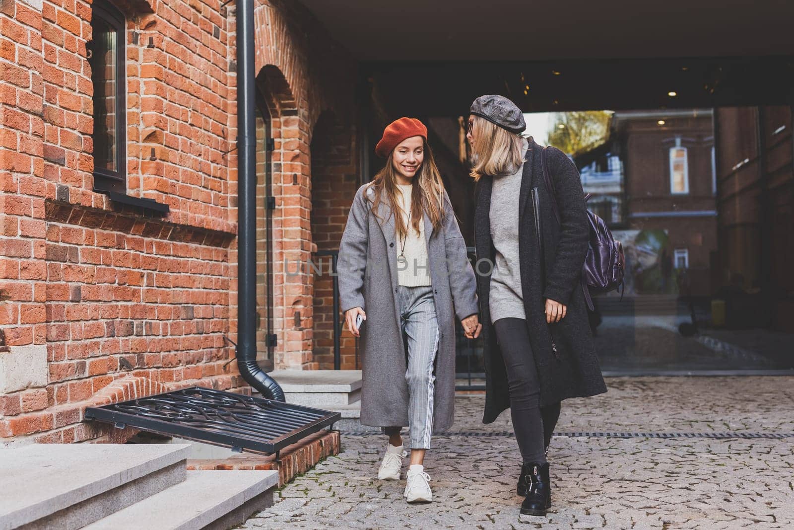 Two girls walking on street together and holding their hands. They are wearing spring or autumn clothes and they happy. Friendship and relationship concept