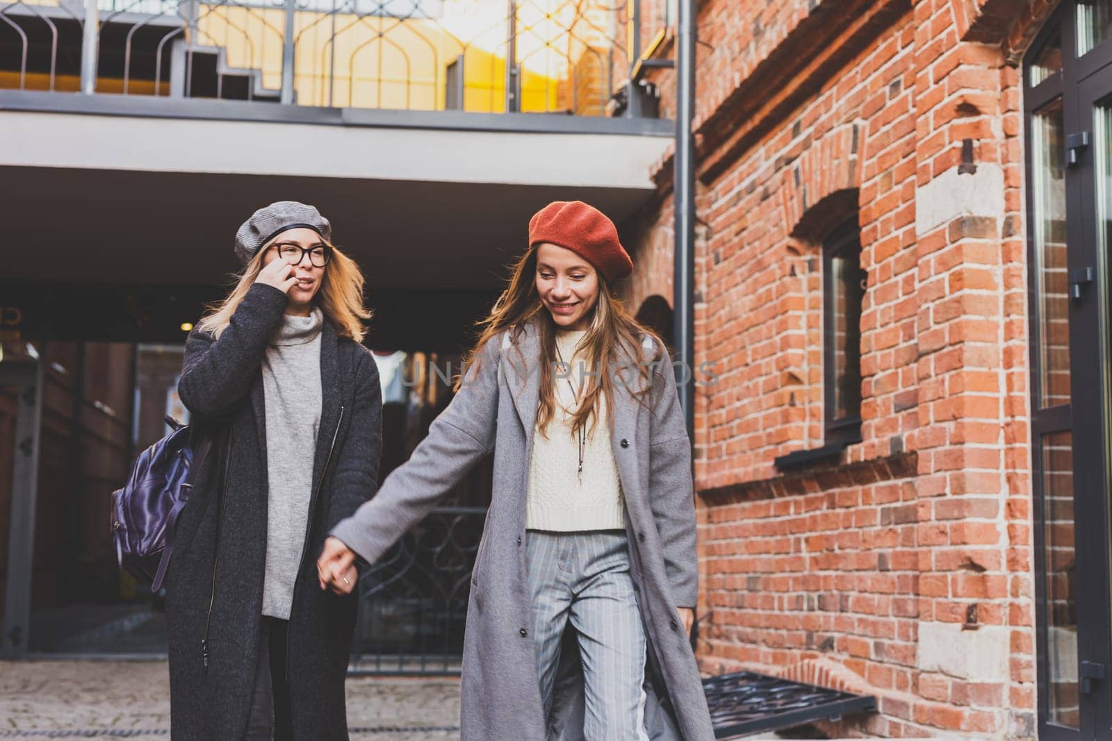 Funny female friends laughing in autumn day. Lovely girls in black coat and girl in gray coat having fun on city background. Friendship and female love concept. Copy space by Satura86