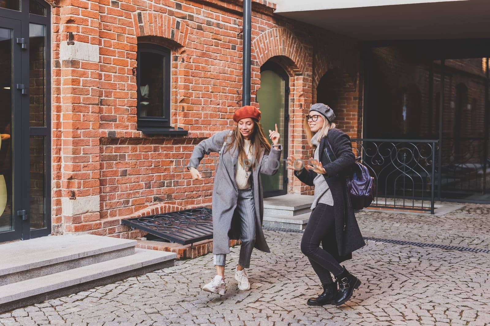 Millennial young women having fun and dance on city street. Female friends enjoying autumn day around the city.