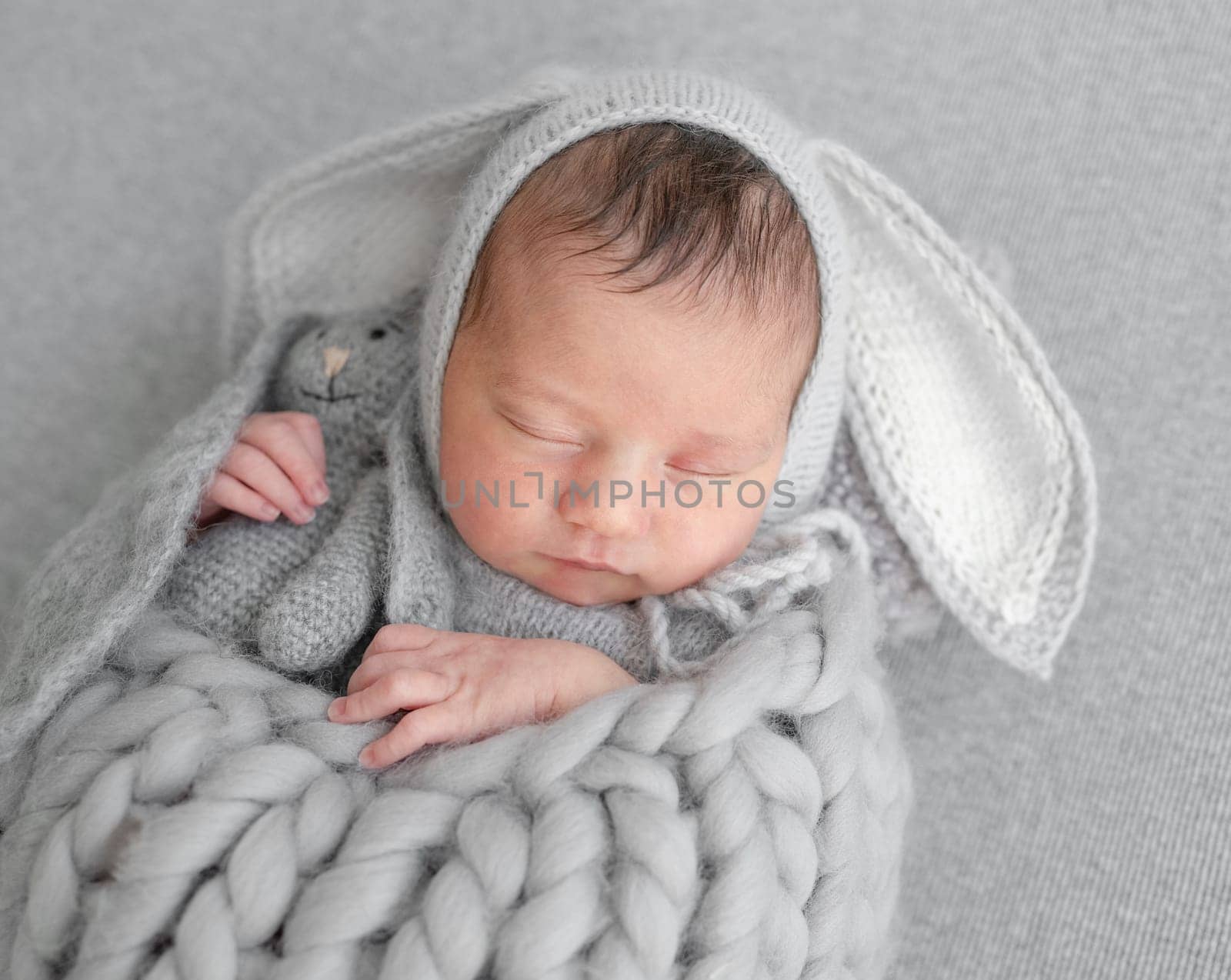 Newborn Girl In Bunny Hat Sleeps During Baby Photo Session In Studio