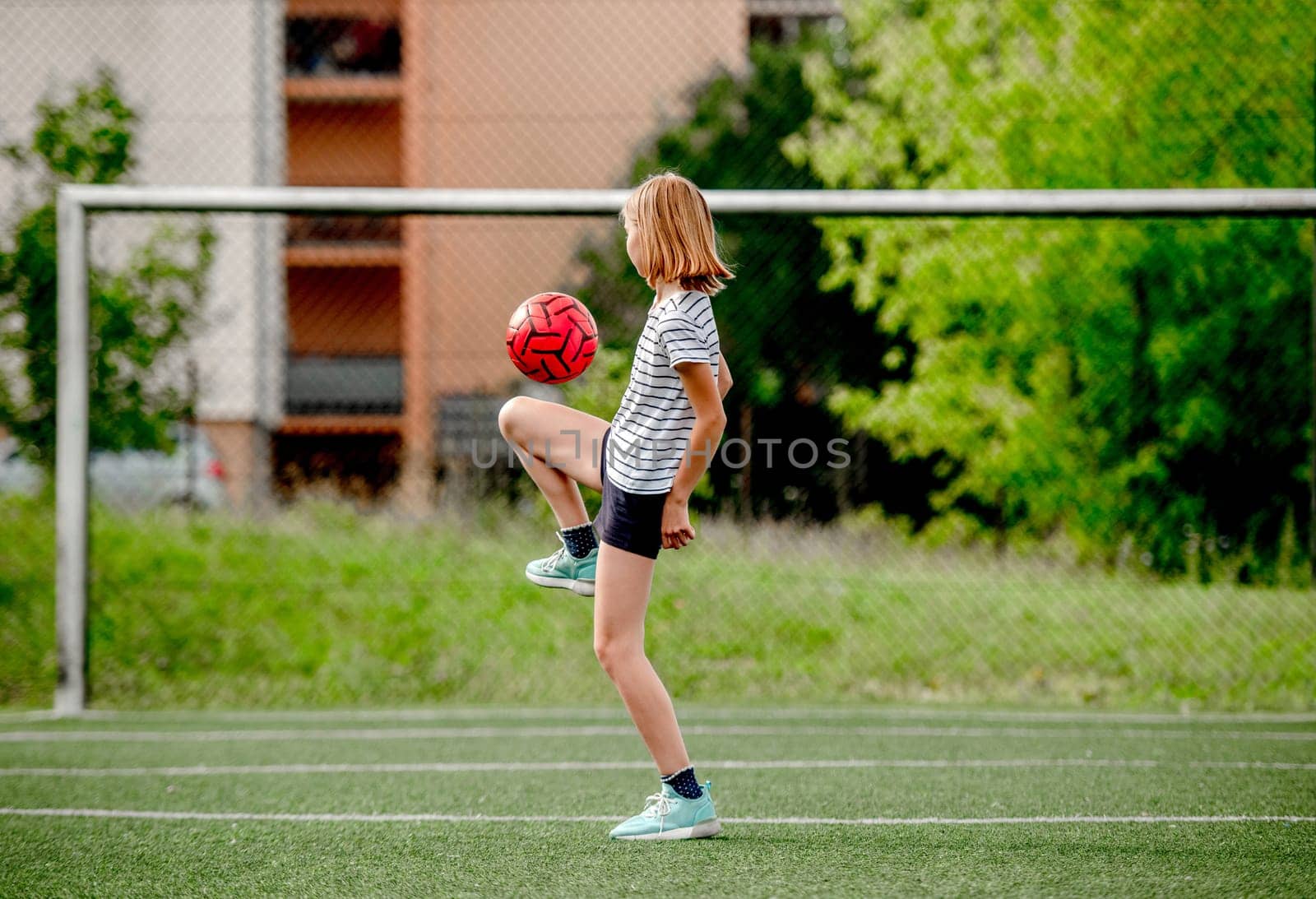 Pretty child girl kicking football ball at socket field. Cute female kid playing active game