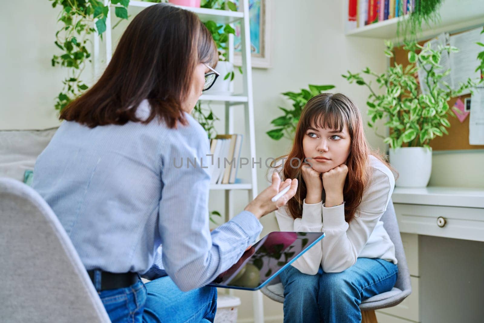 Sad, serious teenage girl at a session in the office of a mental professional, psychologist, counselor, social worker. Feelings, difficulties, problems, depression, stress, youth concept