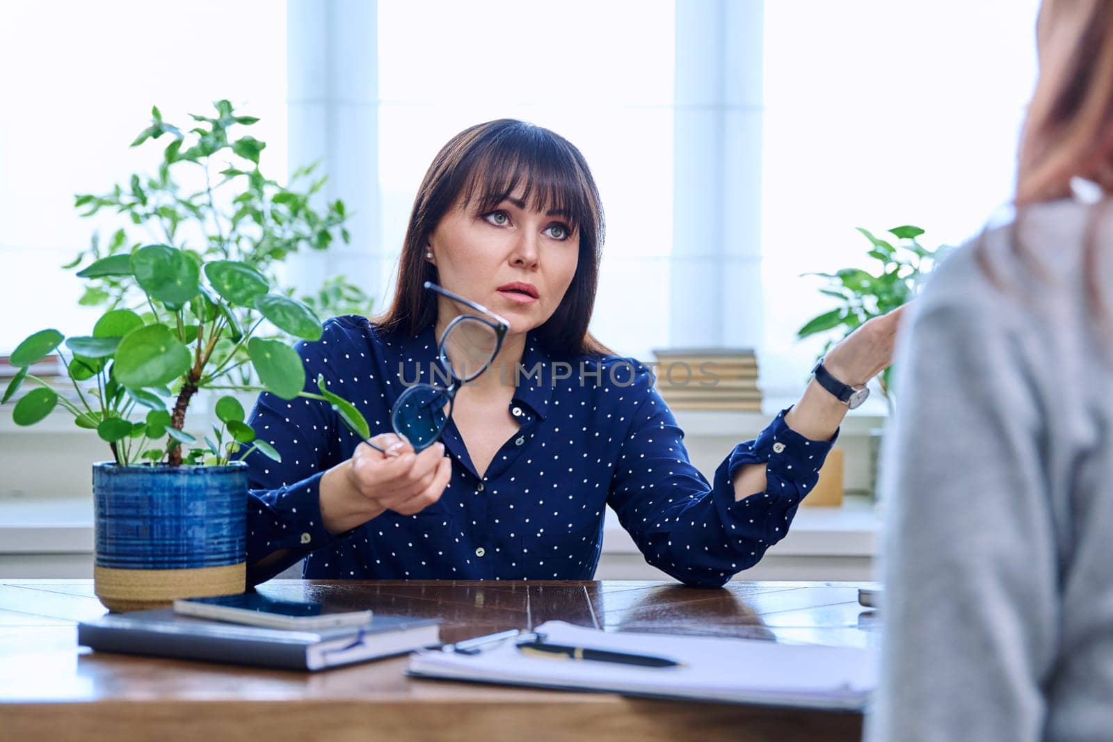 Mature sad woman in therapy session with mental professional psychologist, sitting at table in office of therapist counselor social worker. Psychology psychotherapy mental assistance treatment support