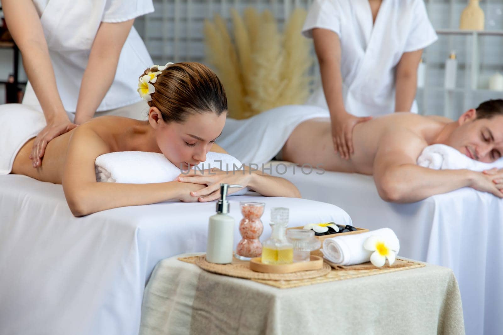 Caucasian couple customer enjoying relaxing anti-stress spa massage and pampering with beauty skin recreation leisure in day light ambient salon spa at luxury resort or hotel. Quiescent