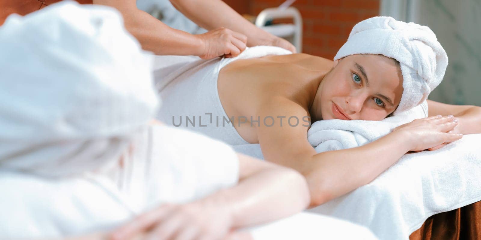 A portrait of two attractive young women with beautiful skin in white towel having a back massage by professional masseur at traditional spa salon. Beauty and healthy. Tranquility.