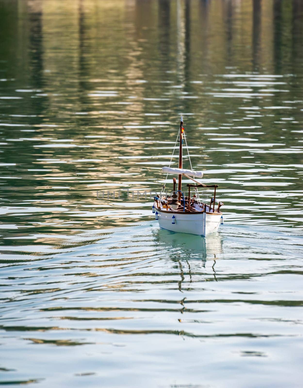 A model sailboat embarks on a serene journey across the tranquil waters, its sails unfurled and catching the soft light. This charming scene captures the playful essence of nautical hobbies and the peaceful joy of a calm lake