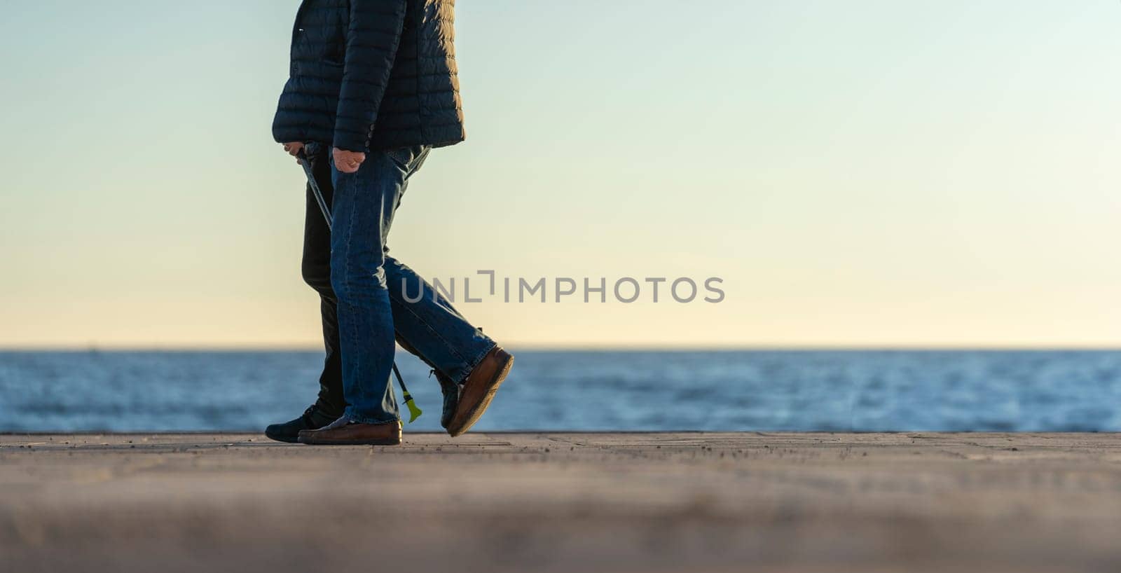 The focus is on the steps of a solitary figure taking a walk along the coast, with the ocean horizon stretching endlessly in the background during the tranquil moments of dusk