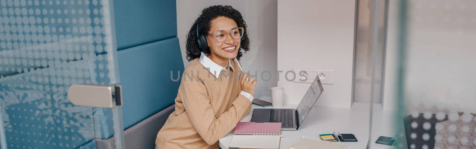 Stylish business woman in eyeglasses and headphones working on laptop while sitting in office by Yaroslav_astakhov