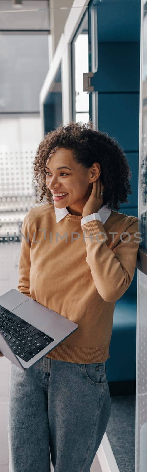 Young smiling female manager using laptop while standing on modern office background by Yaroslav_astakhov