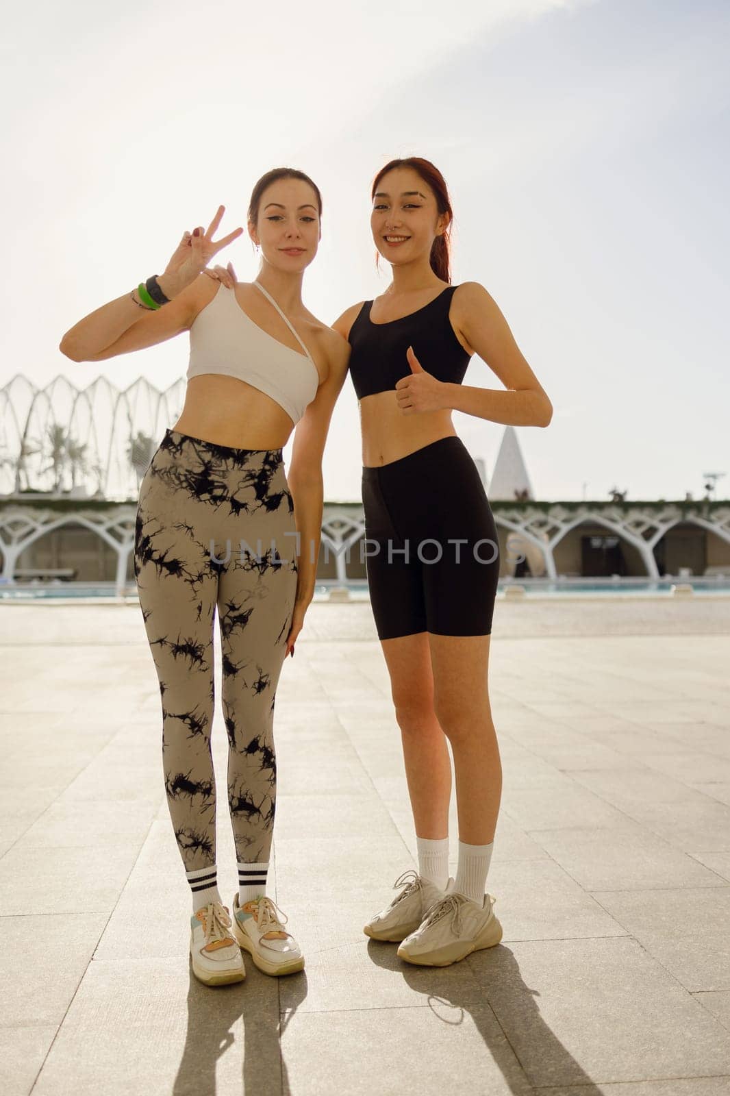 Two young female sportswomen have a rest after morning jogging outdoors and looks camera with smile