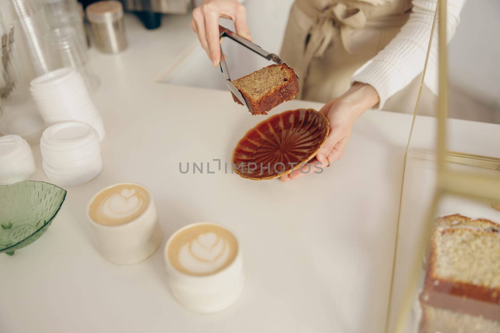 The waitress's hand puts the piece of cupcake on the table at a cafe standing behind bar counter