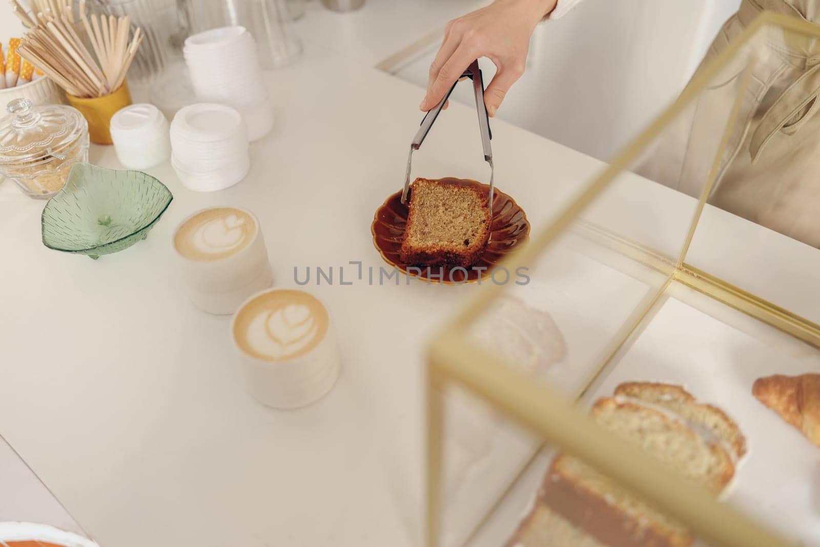 Close-up of female waitress hands putting a delicious dessert on a plate standing behind bar counter by Yaroslav_astakhov