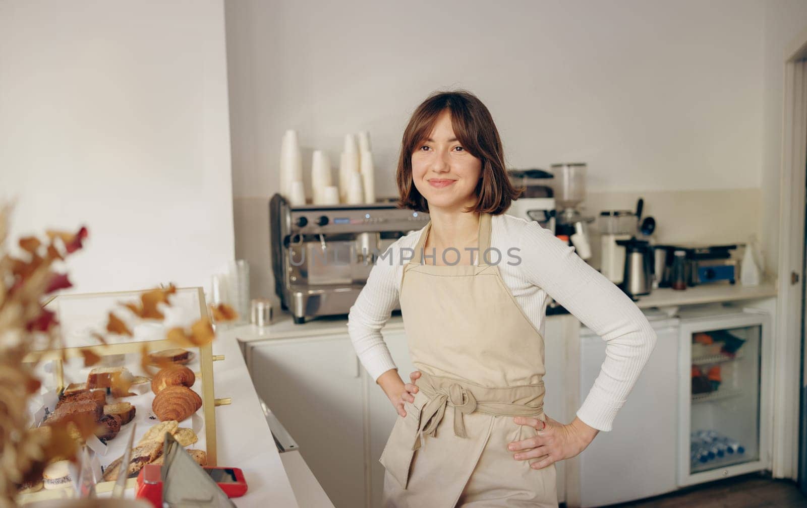 Beautiful female barista is looking at camera and smiling while standing near bar counter in cafe by Yaroslav_astakhov
