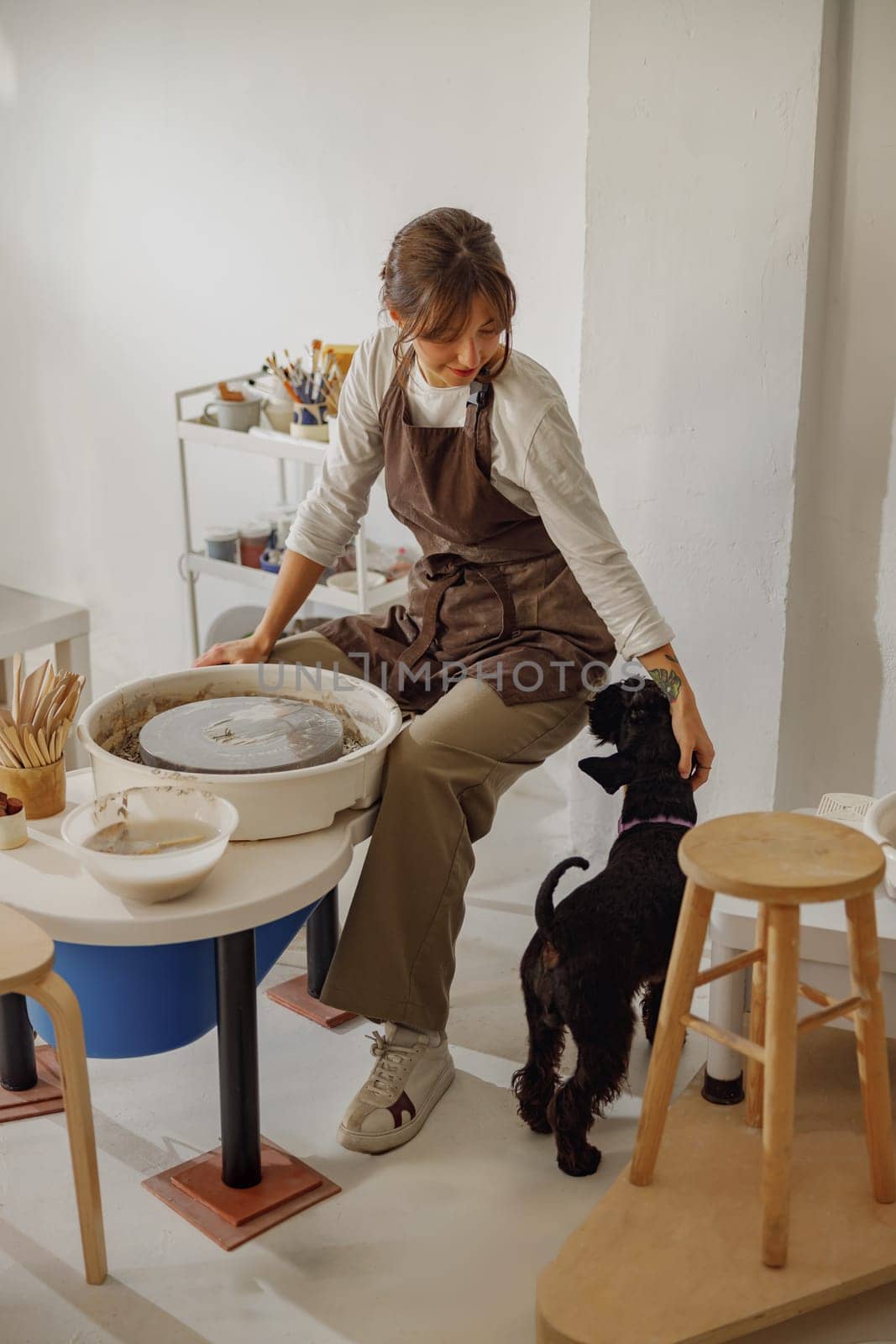 Smiling female ceramist with her dog working in pottery studio. High quality photo