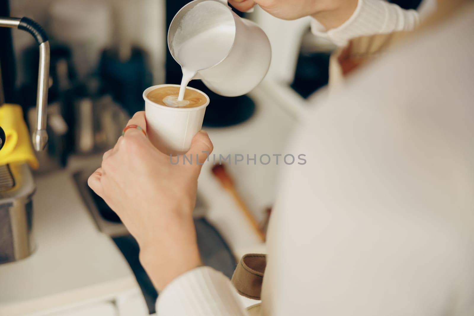 Close up of female barista makes coffee and pours it into a mug while working in coffee shop by Yaroslav_astakhov