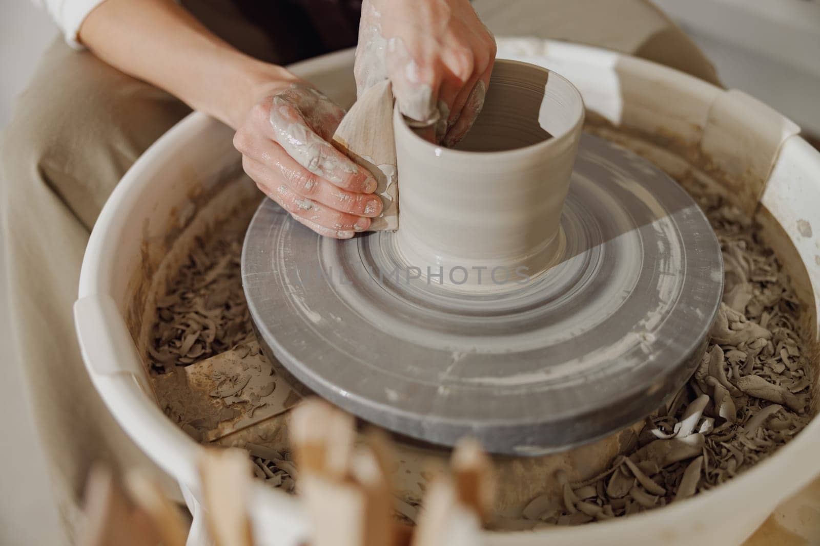 Female potter in apron making shape of clay vase on spinning pottery tool in ceramic workshop