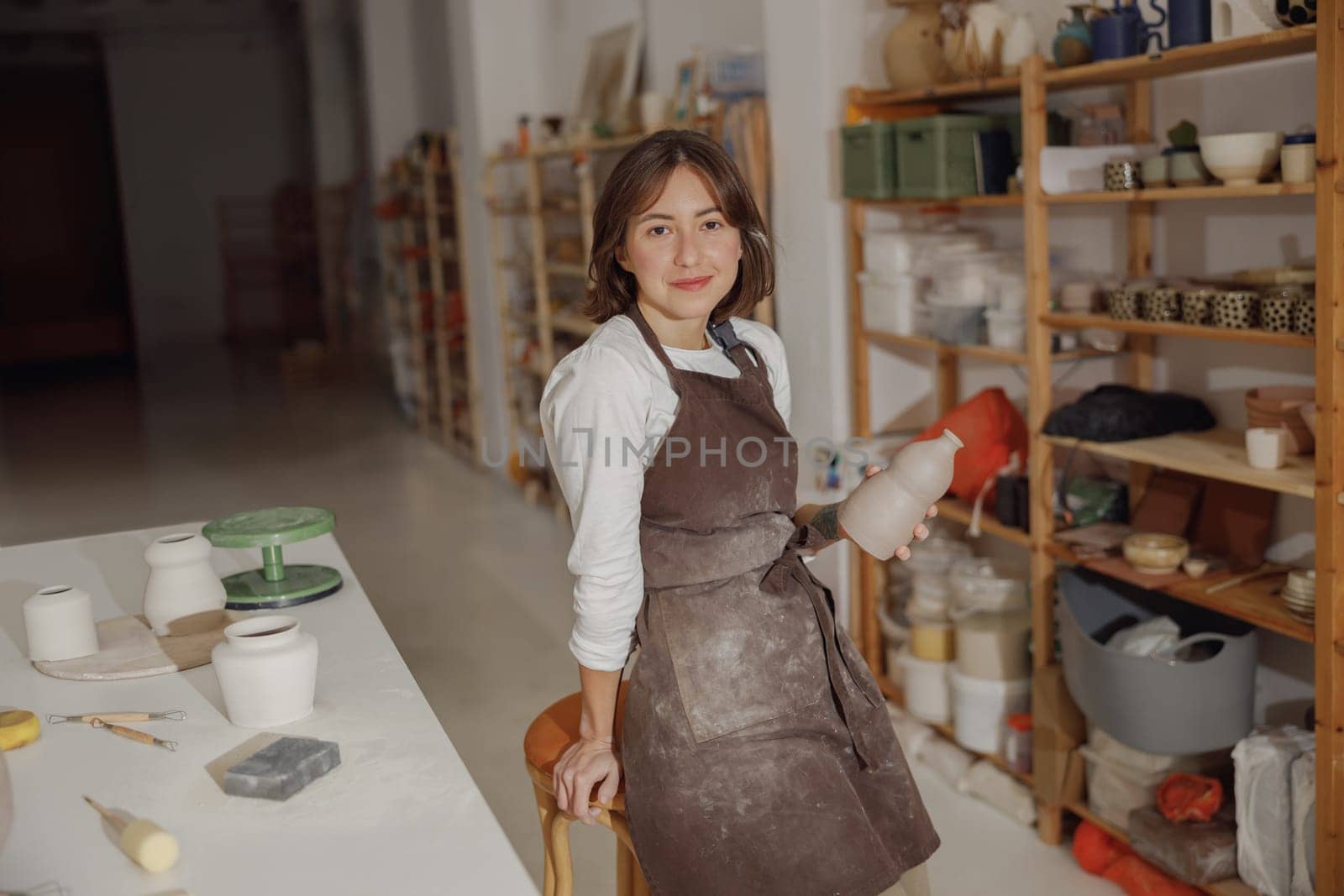 Smiling entrepreneur crafts woman holding mug in pottery studio while looking at camera by Yaroslav_astakhov