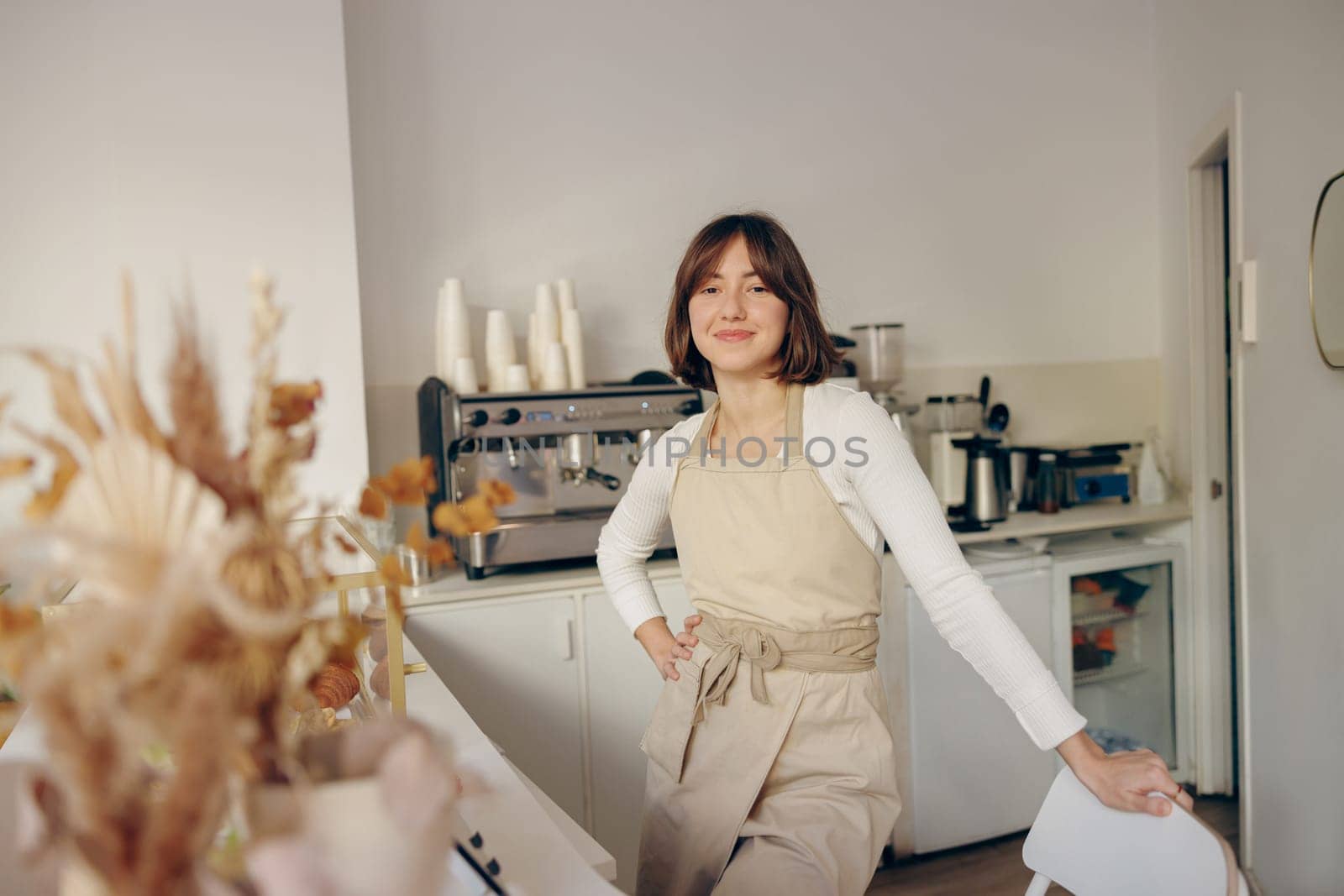 Beautiful female barista is looking at camera and smiling while standing near bar counter in cafe