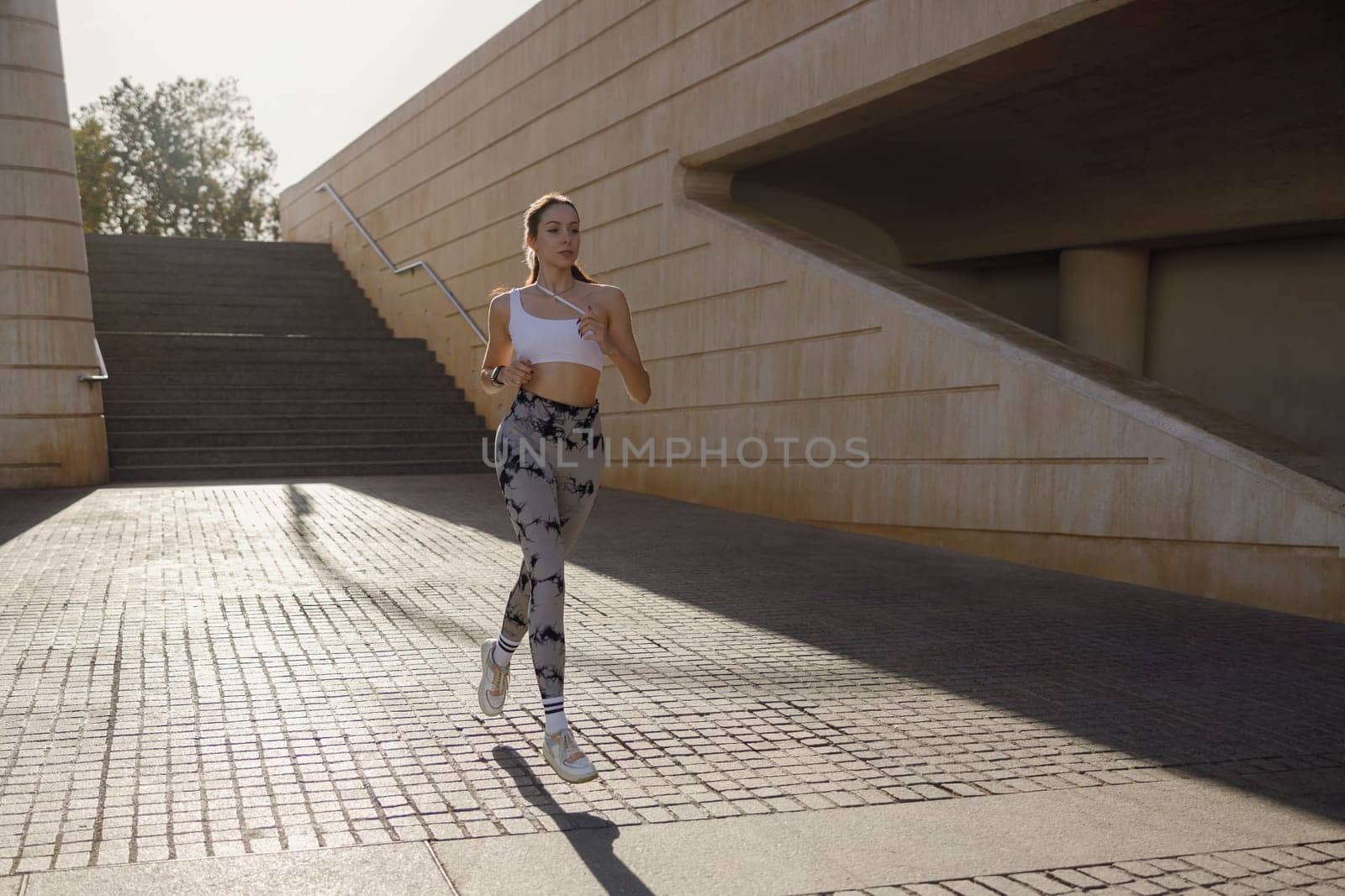 Active woman athlete is jogging on morning on modern building background. Healthy life concept