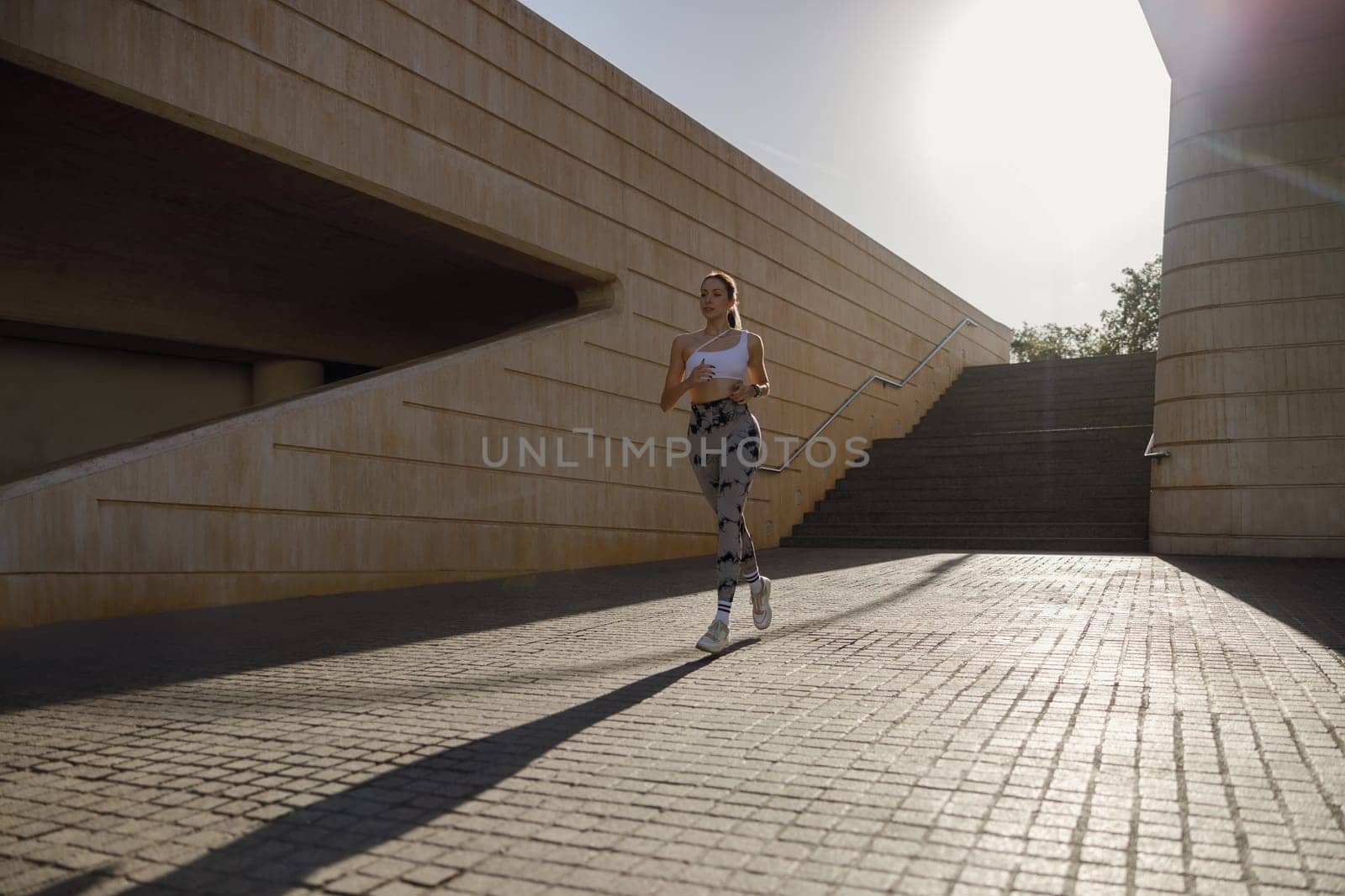 Young woman in sportswear is running on modern buildings background. Active lifestyle concept