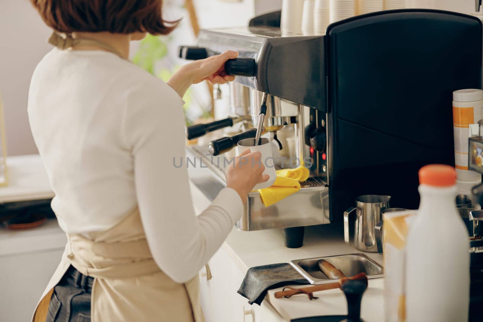 Close up of female barista frothing milk for coffee with professional coffeemaker working in cafe