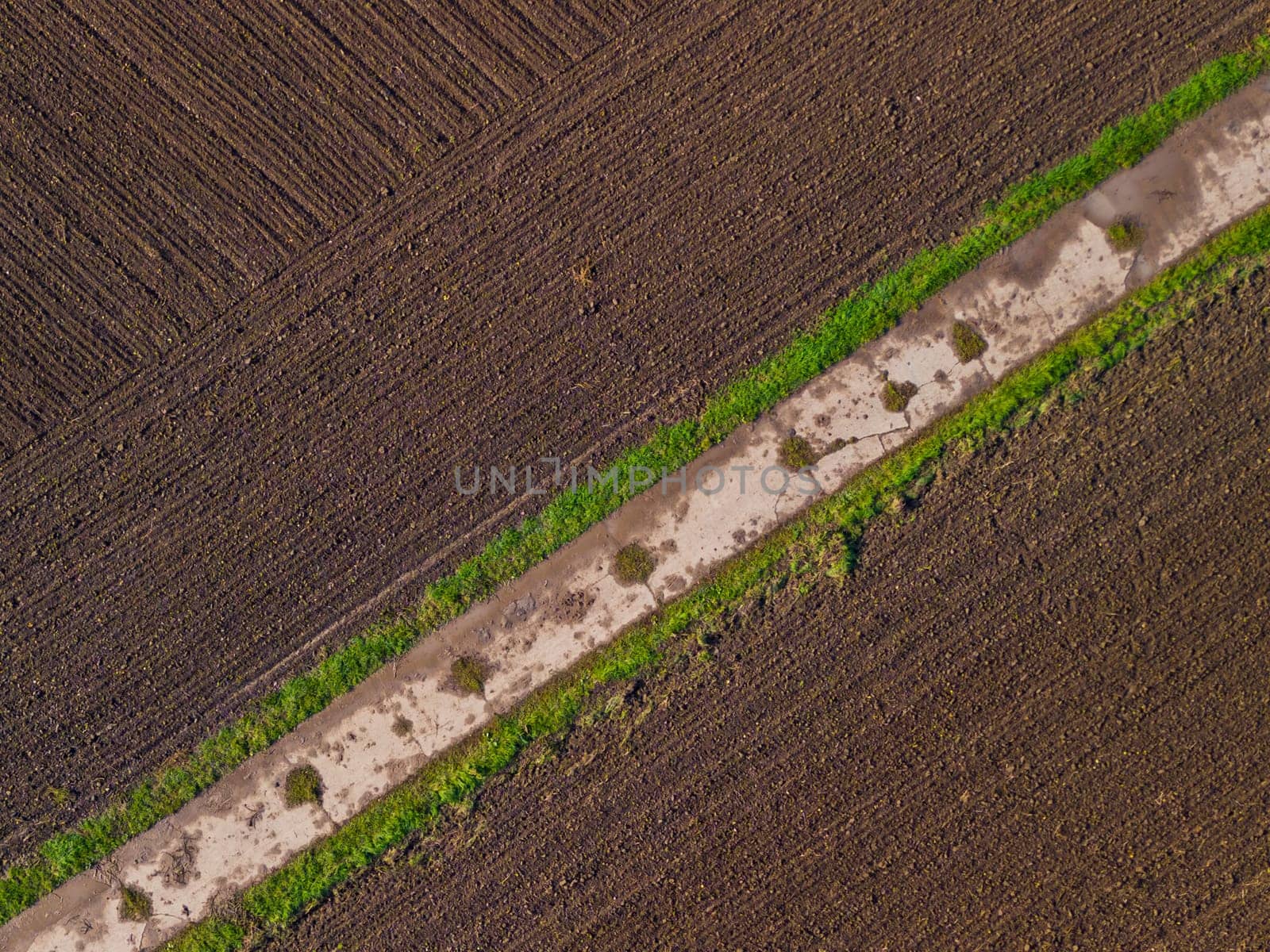 Aerial view with farm track between wet soil on a field by astrosoft