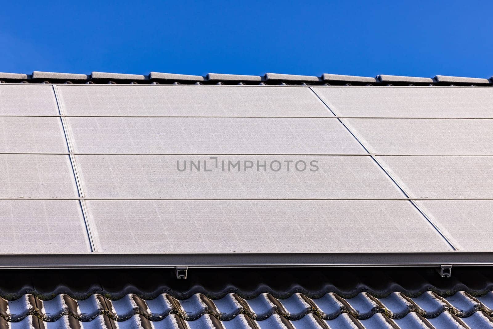 A house roof with iced solar panels in sunshine by astrosoft