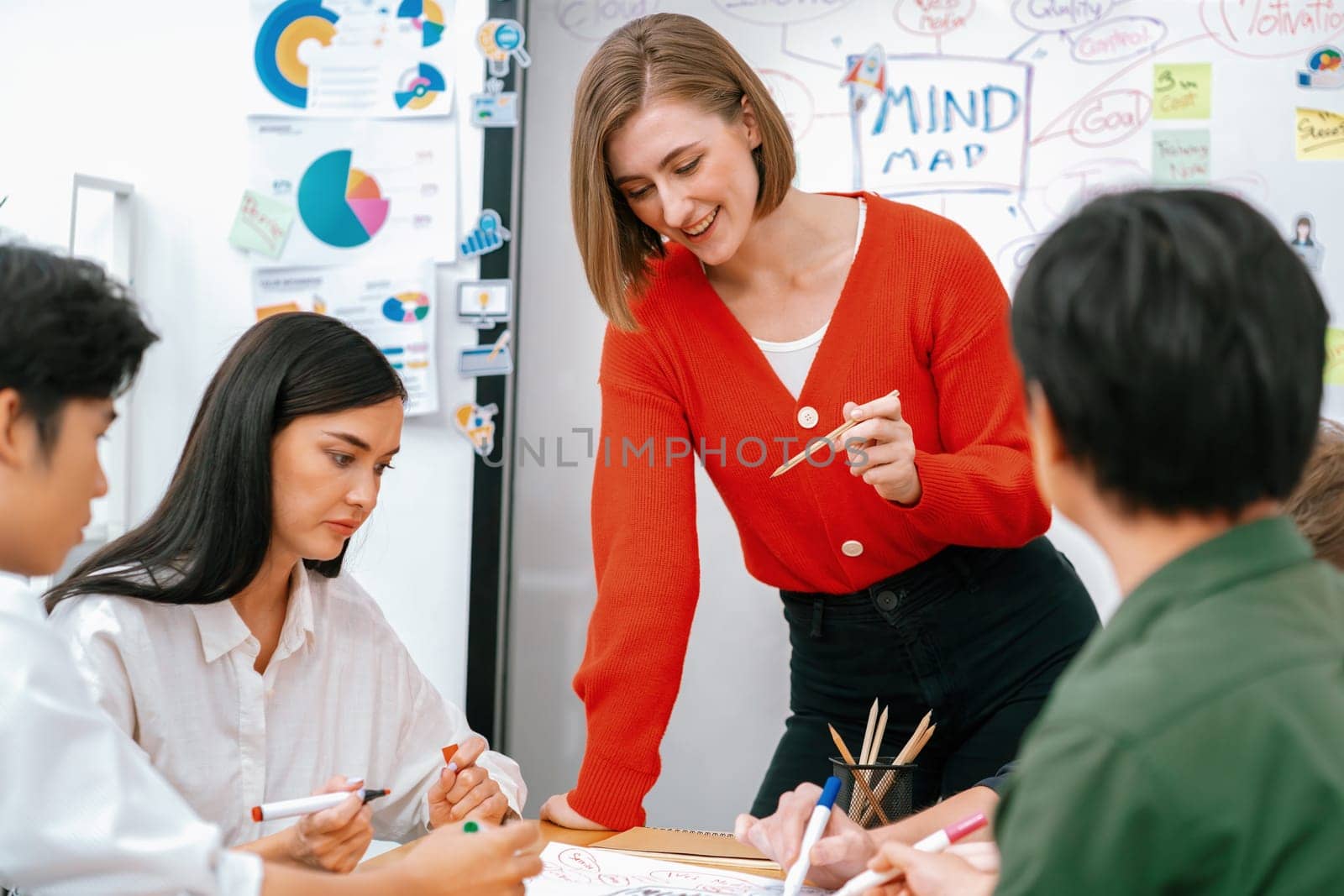 Creative happy business team brainstorming and sharing idea by using mind map and graphic graph while young beautiful project manager pointing at important point at business meeting. Immaculate.