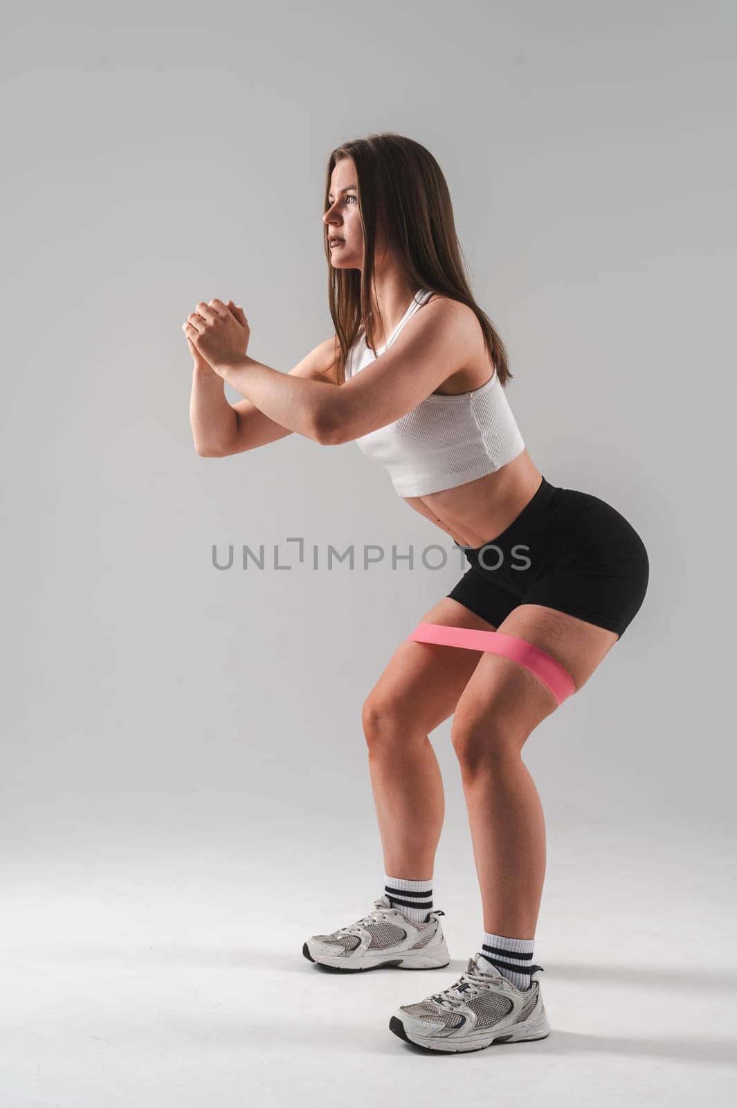 Caucasian woman doing squats with fitness band on white background. Vertical photo. by mrwed54