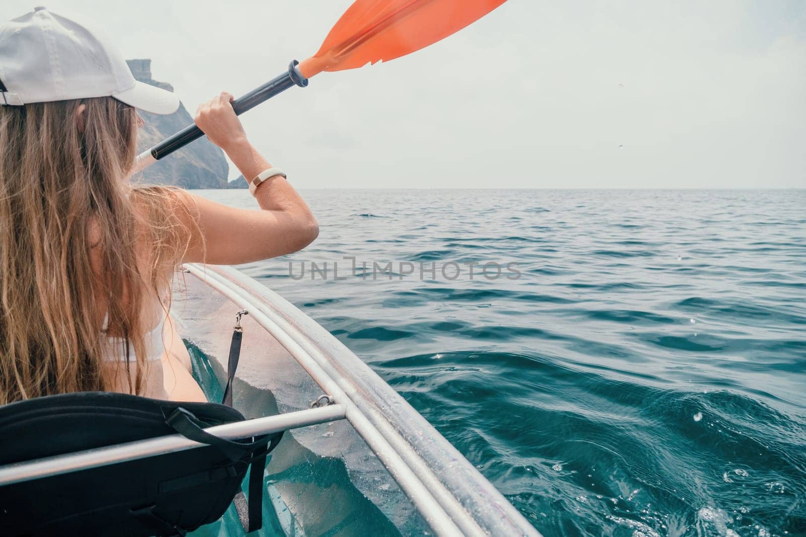 Woman in kayak back view. Happy young woman with long hair floating in transparent kayak on the crystal clear sea. Summer holiday vacation and cheerful female people having fun on the boat.