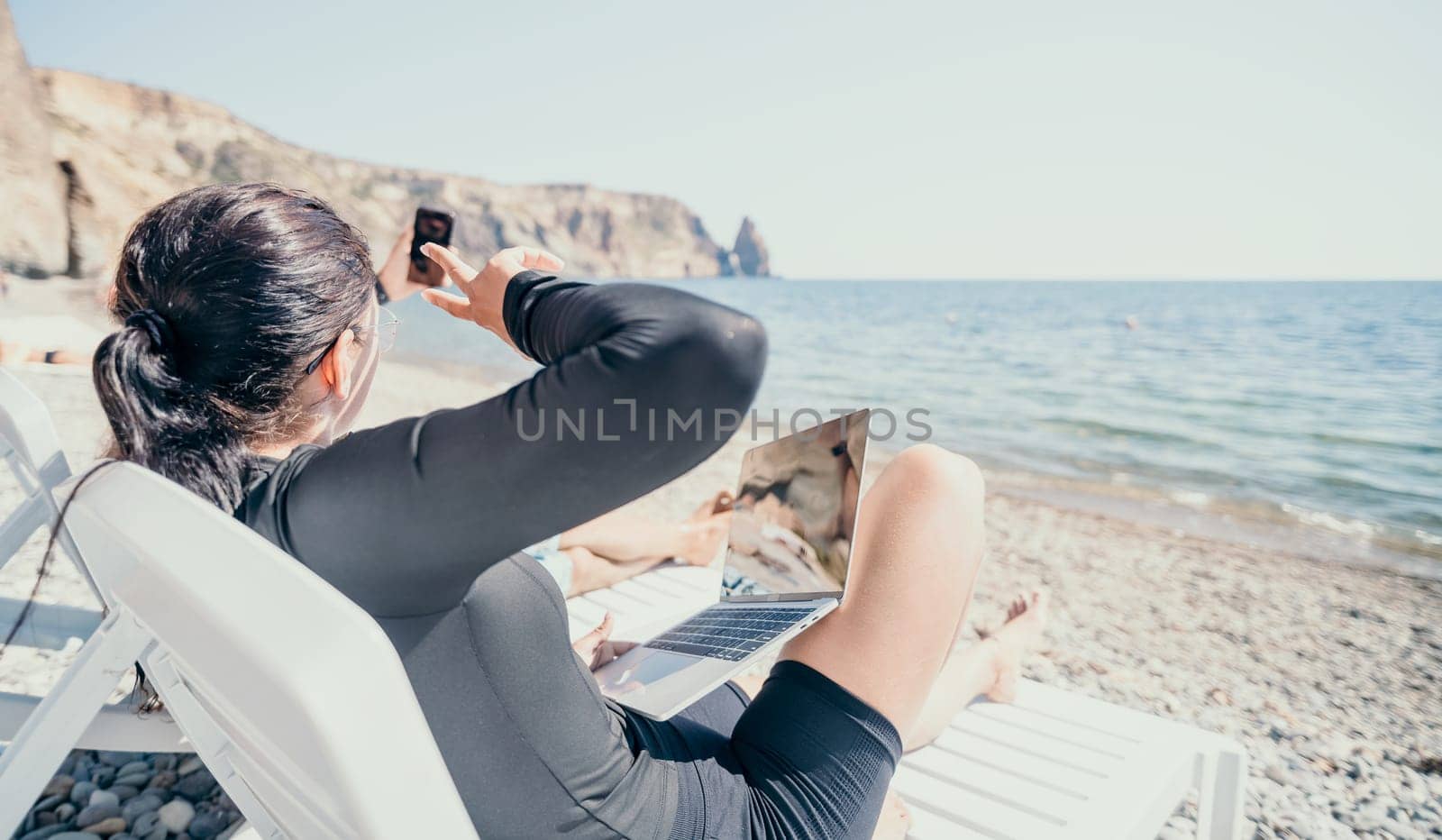 Digital nomad, Business man working on laptop by the sea. Man typing on computer by the sea at sunset, makes a business transaction online from a distance. Freelance, remote work on vacation