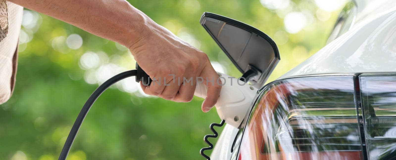 Young man recharge electric car's battery from charging station. Expedient by biancoblue