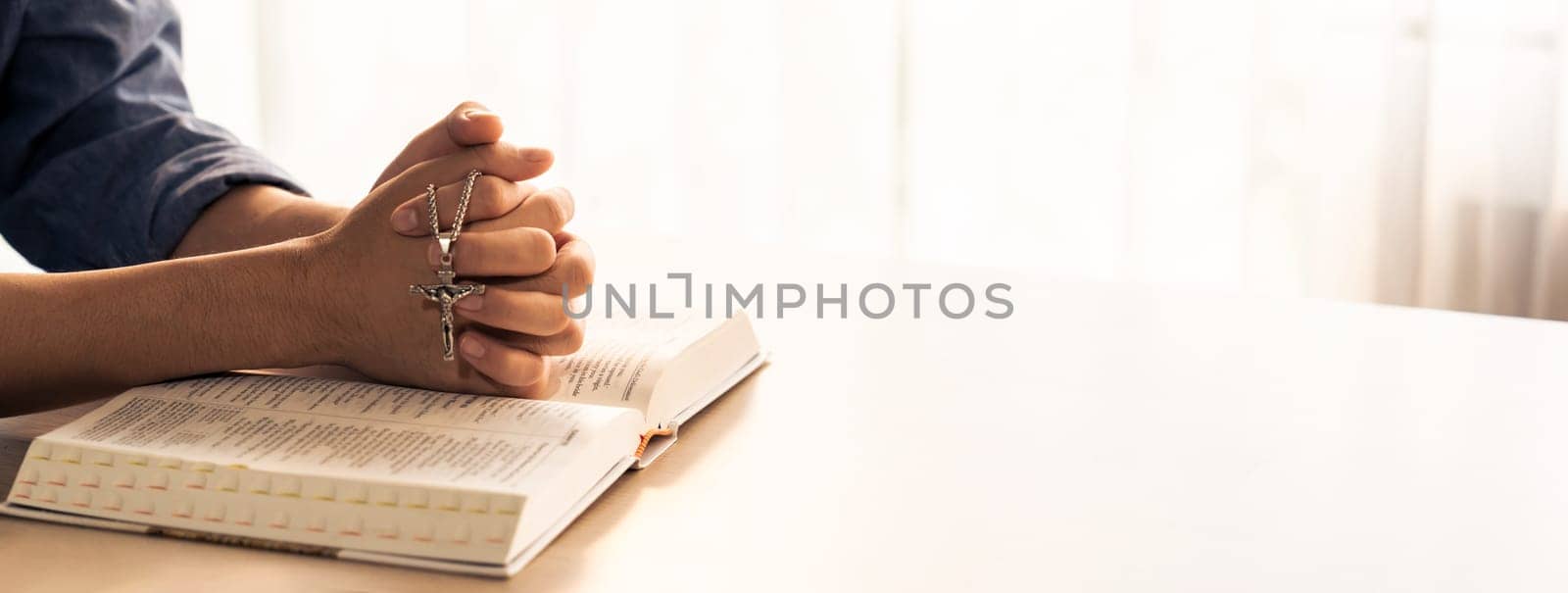 Asian male folded hand prayed on holy bible book while holding up a pendant crucifix. Spiritual, religion, faith, worship, christian and blessing of god concept. Blurring background. Burgeoning.