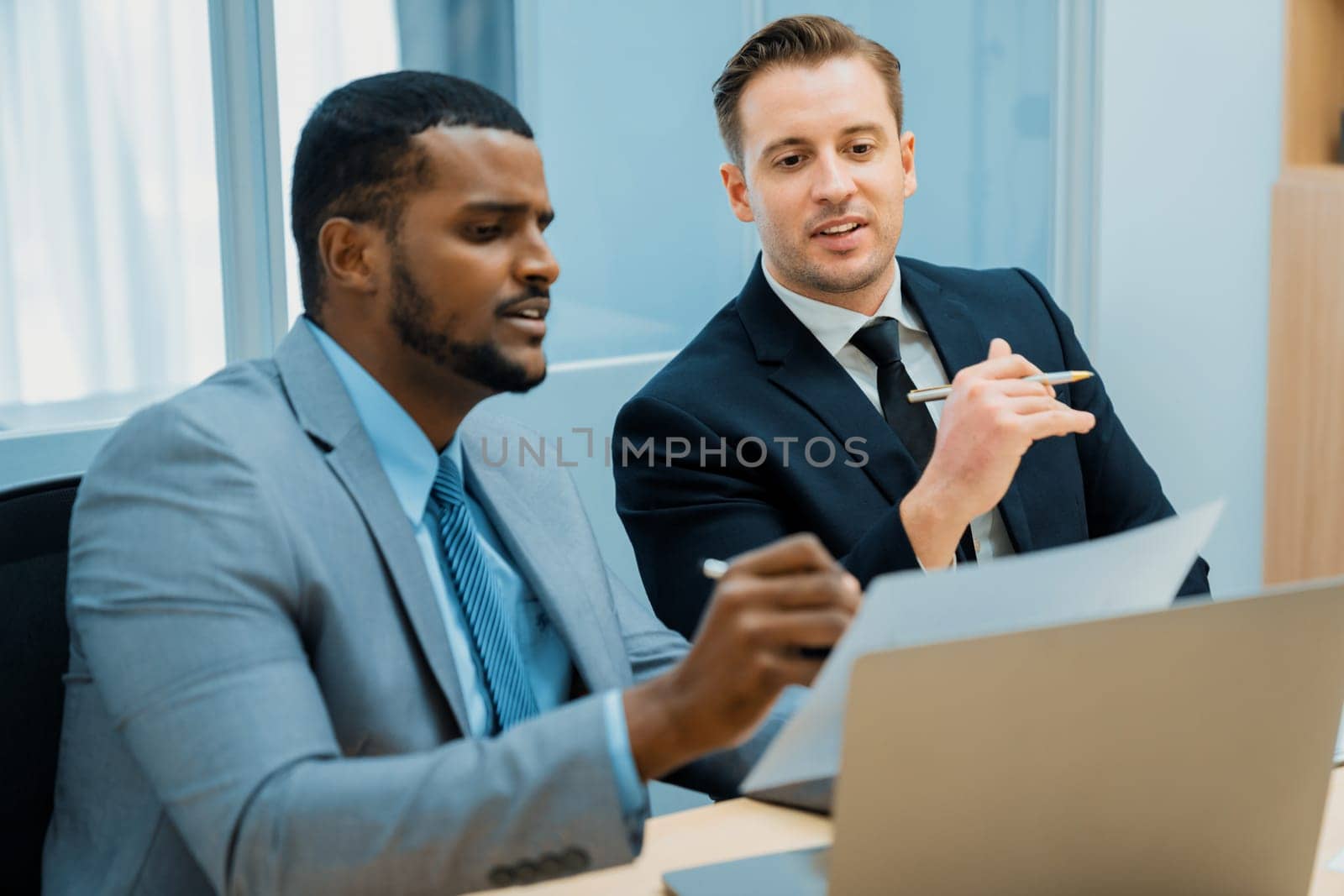 African male leader explain strategy while show solution to professional project manager by pointing at document, using laptop. Skilled business team brainstorming idea. Business meeting. Ornamented.