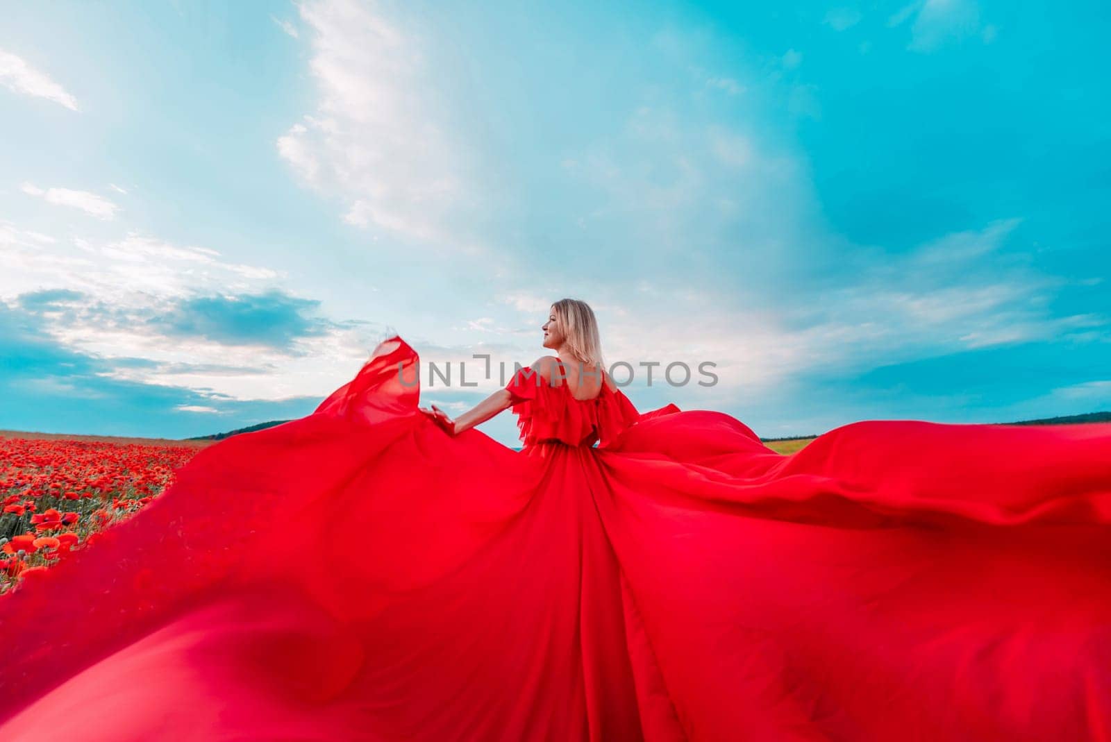 Woman poppy field red dress. Happy woman in a long red dress in a beautiful large poppy field. Blond stands with her back posing on a large field of red poppie