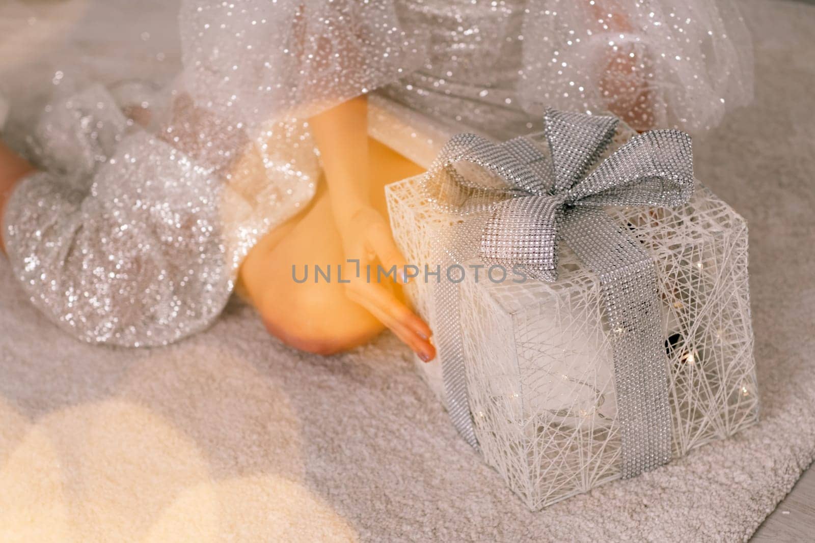 A beautiful box with a gift in the hands of a girl, she sits in a brilliant dress and holds it in her hands. Bokeh from garlands