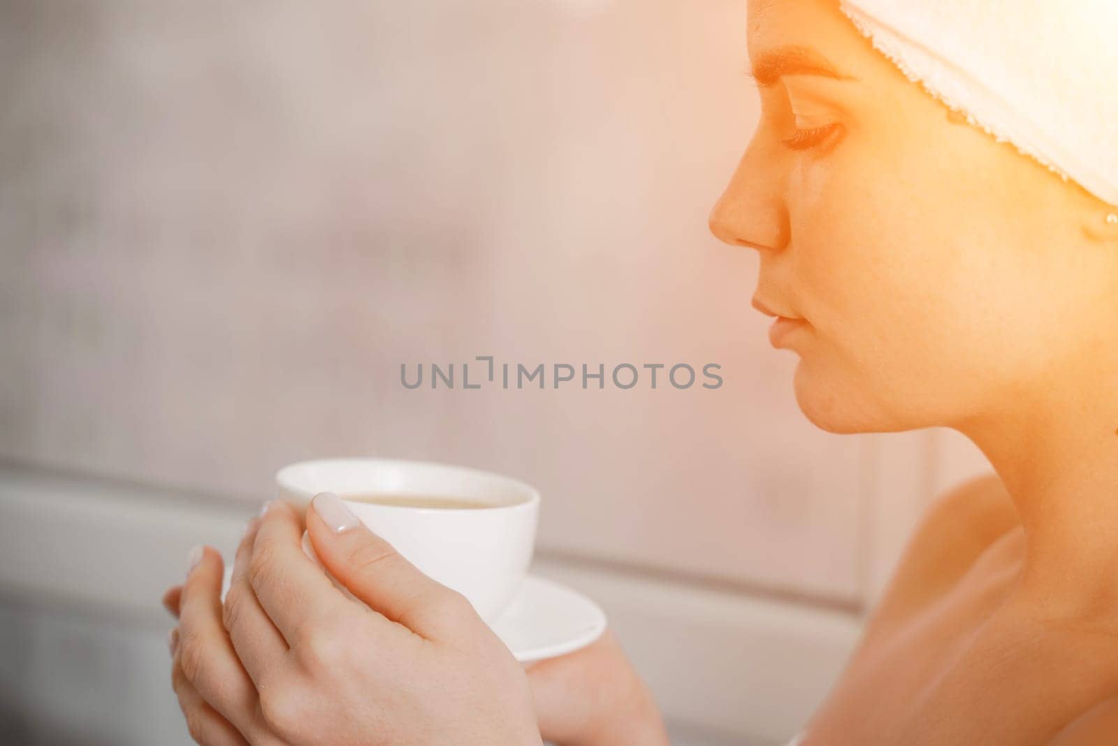 Young serene relaxed woman in spa bath towel drinking hot beverage tea coffee after taking shower bath at home. Beauty treatment, hydration concept. by Matiunina