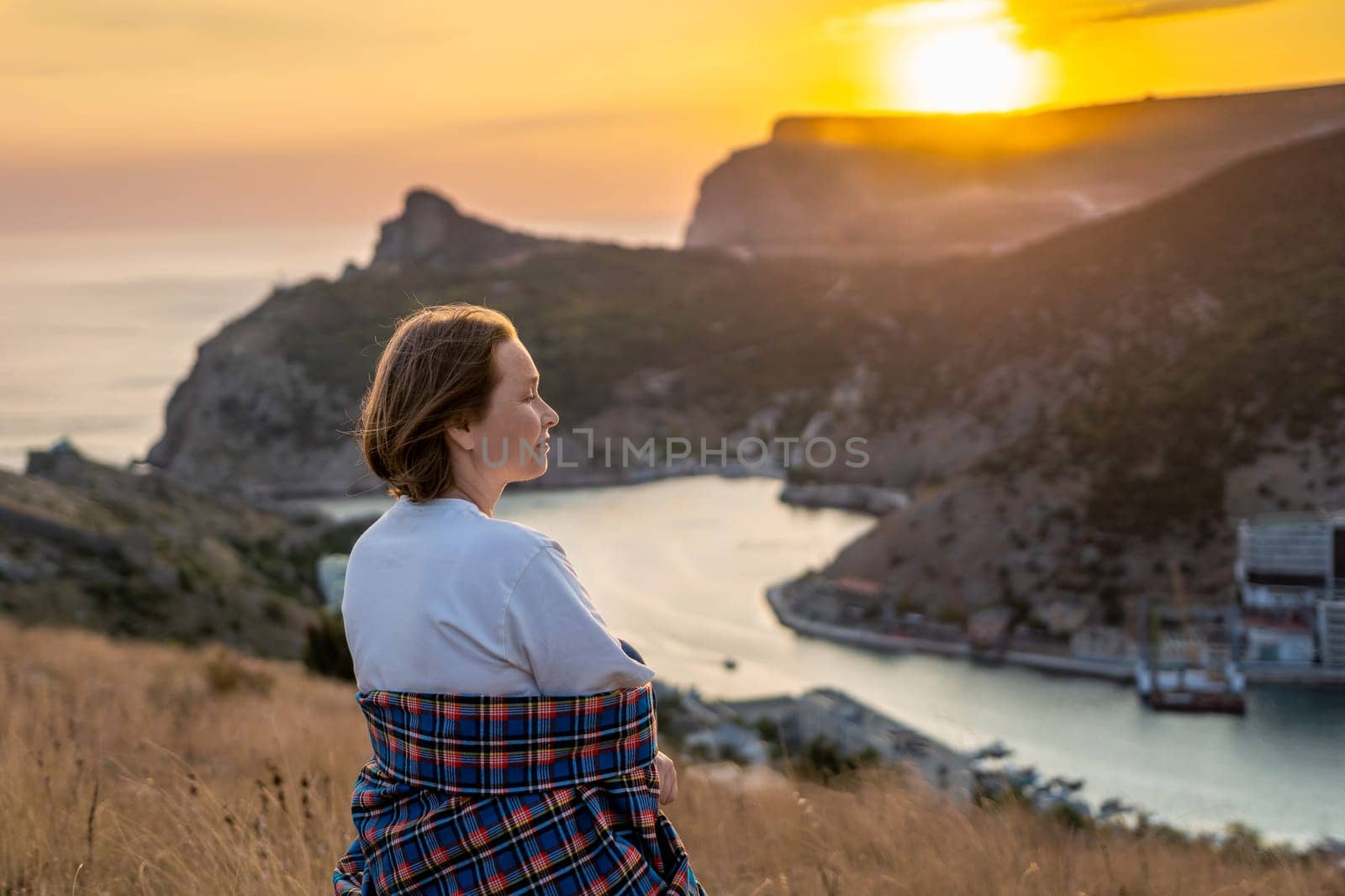 Happy woman on sunset in mountains. Woman siting with her back on the sunset in nature in summer. Silhouette. by Matiunina