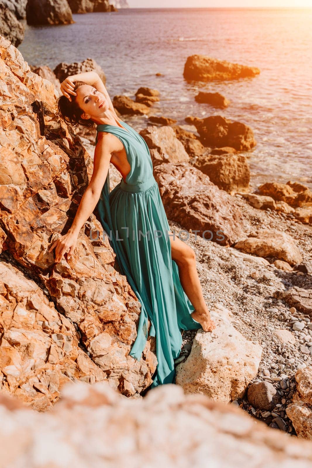 Woman green dress sea. Woman in a long mint dress posing on a beach with rocks on sunny day. Girl on the nature on blue sky background