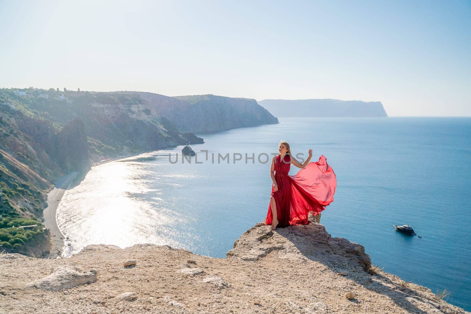 A woman in a red flying dress fluttering in the wind, against the backdrop of the sea