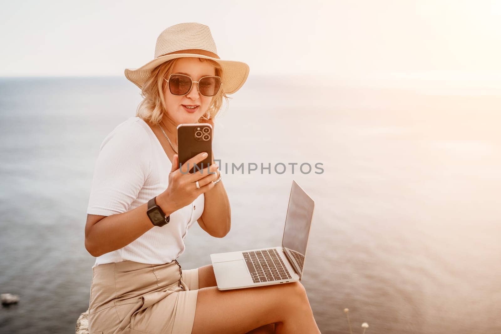 Digital nomad, Business woman working on laptop by the sea. Pretty lady typing on computer by the sea at sunset, makes a business transaction online from a distance. Freelance, remote work on vacation by panophotograph