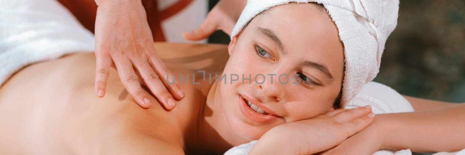 Beautiful young woman received a back massage on a spa bed from professional masseuse. Attractive female relaxes deeply by skilled hands of the massage therapist. Surrounded with nature. Tranquility.